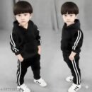 A pair of young children modeling a matching black tracksuit set with white double stripes on the sleeves and pants, wearing white athletic sneakers
